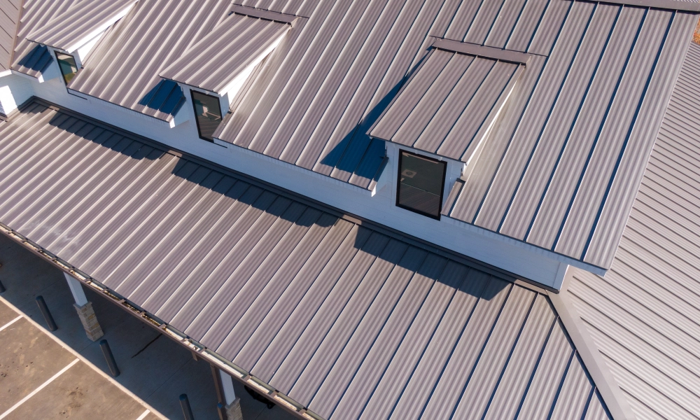 Aerial view of a building with a metal roof, windows, pillars, and a parking lot