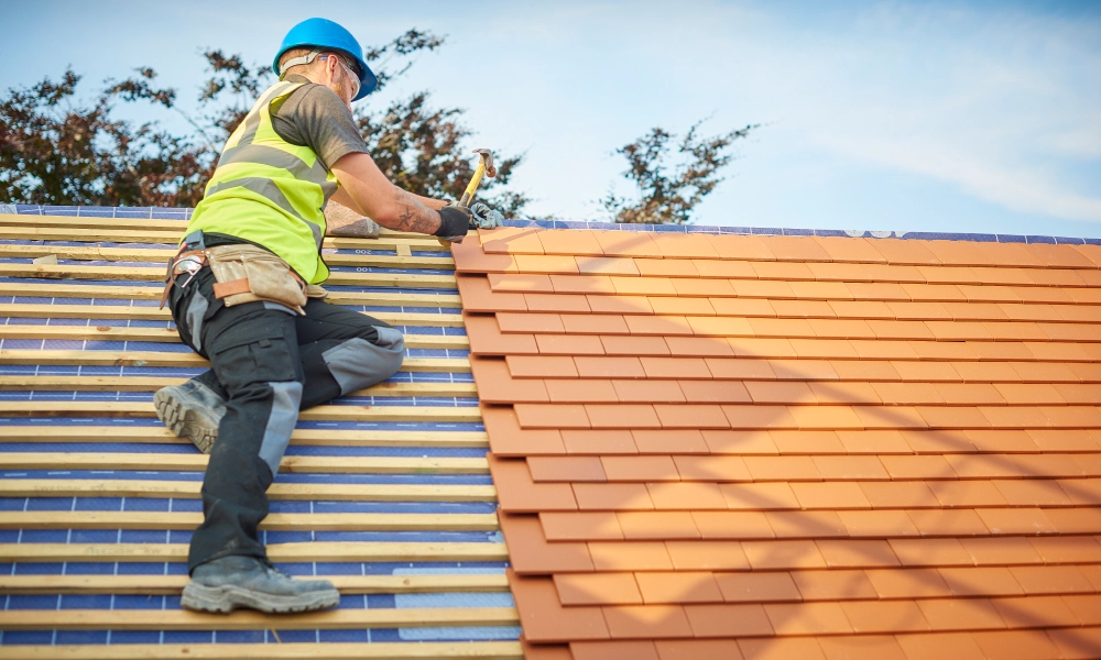Man wearing a helmet and holding a hammer while working on a roof