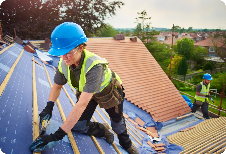 Two men working on a roof with solar panels, surrounded by trees, buildings, and a clear blue sky