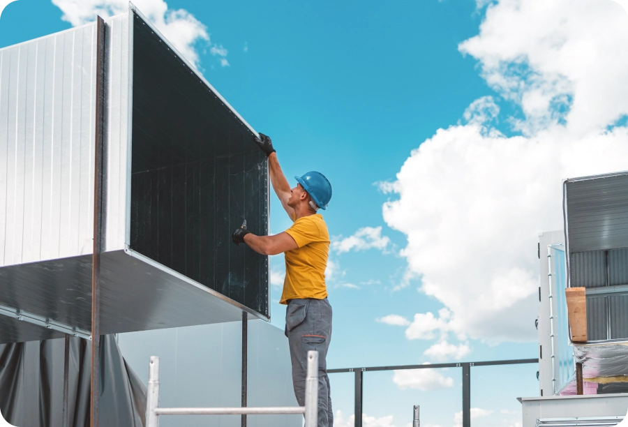 Man in a t-shirt, pants, and a blue helmet standing on a ladder and painting the side of a building