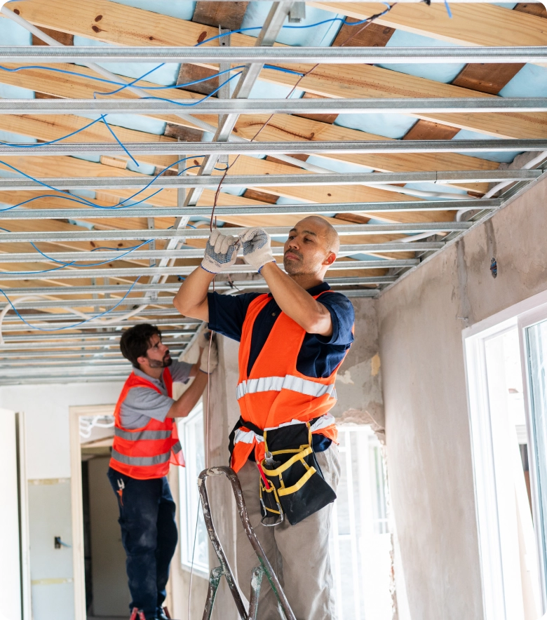Two men in orange vests working on a ceiling, with one of them holding a ladder